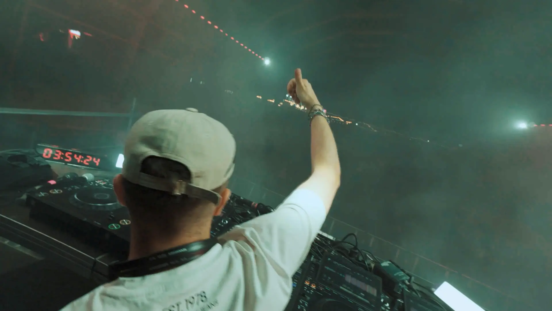 DJ raising a hand above the booth in haze and light