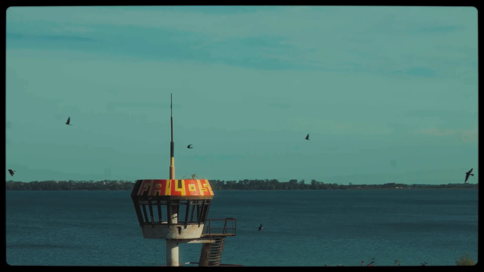 Abandoned lakeside watchtower against a teal sky with birds in flight